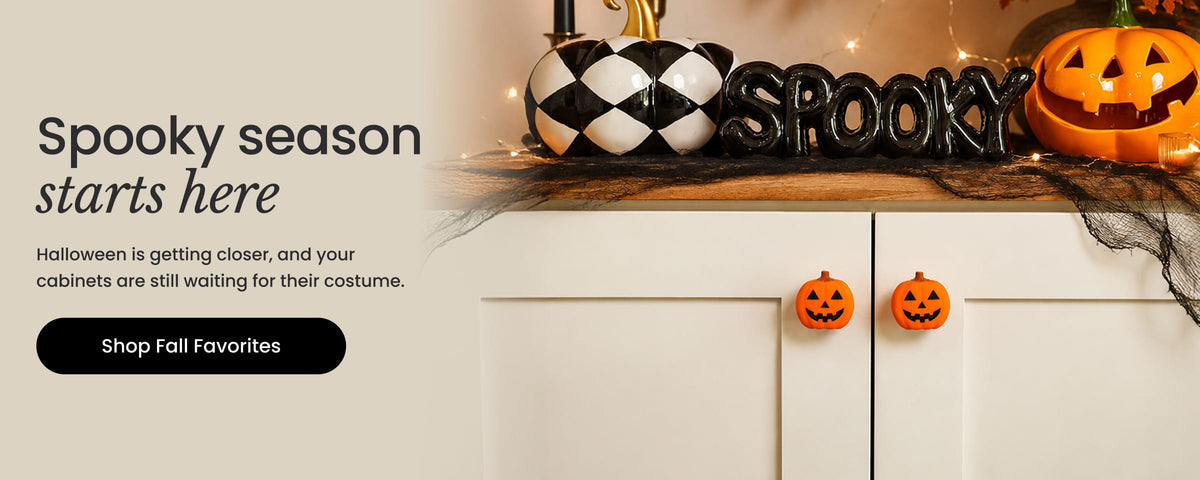 Halloween-themed promotional banner with the text 'Spooky season starts here' and 'Shop Fall Favorites' beside a decorated cabinet topped with jack-o'-lanterns, a black-and-white harlequin pumpkin, and a 'SPOOKY' sign.